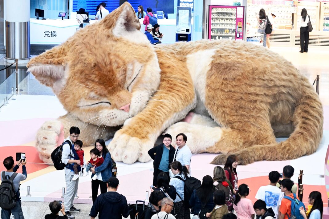 Viajeros tomando fotografías frente a una enorme instalación escultórica de un gato en el aeropuerto de Hong Kong.