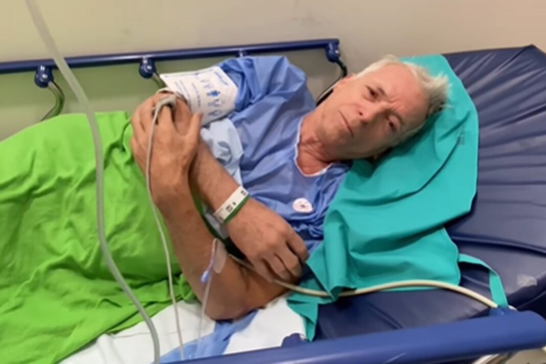Gerardo Romano en una camilla de hospital con bata celeste