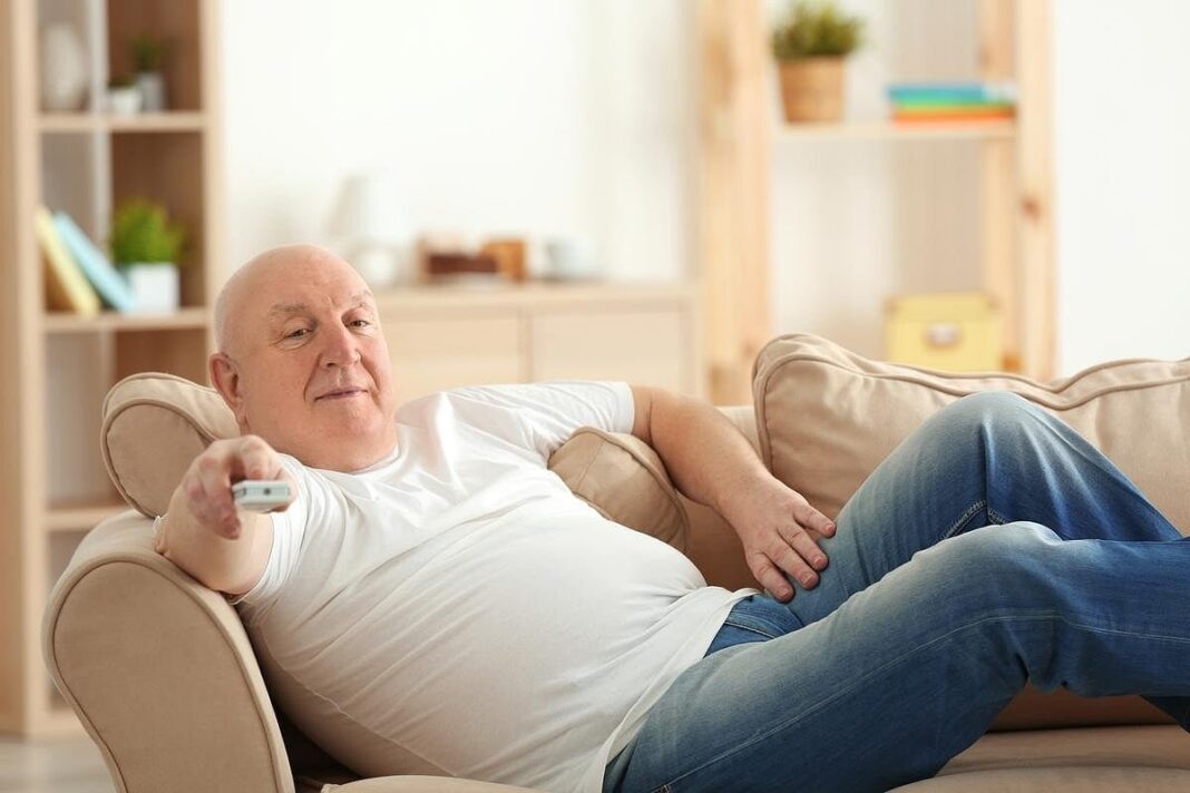 Persona viendo televisión en un sillón, con una resonancia magnética cerebral de fondo