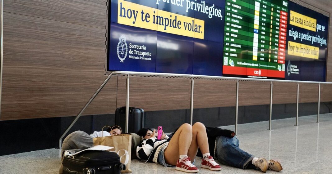 Pasajeros en aeropuerto argentino observando pantalla de partidas y arribos