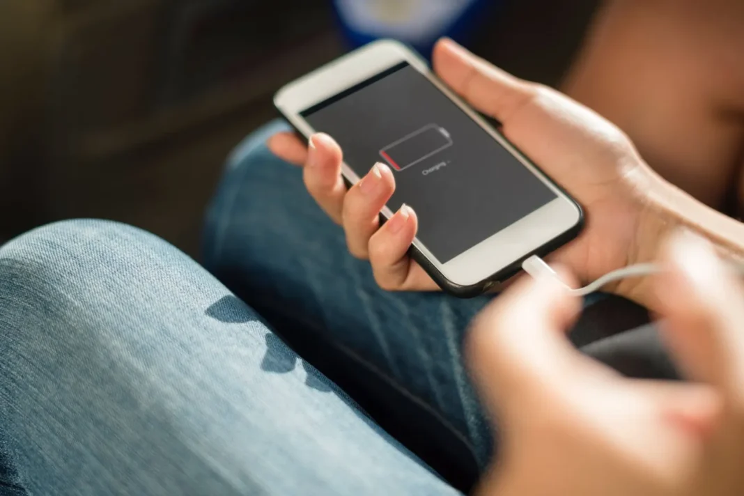Persona cargando un teléfono celular con un cargador conectado a un enchufe
